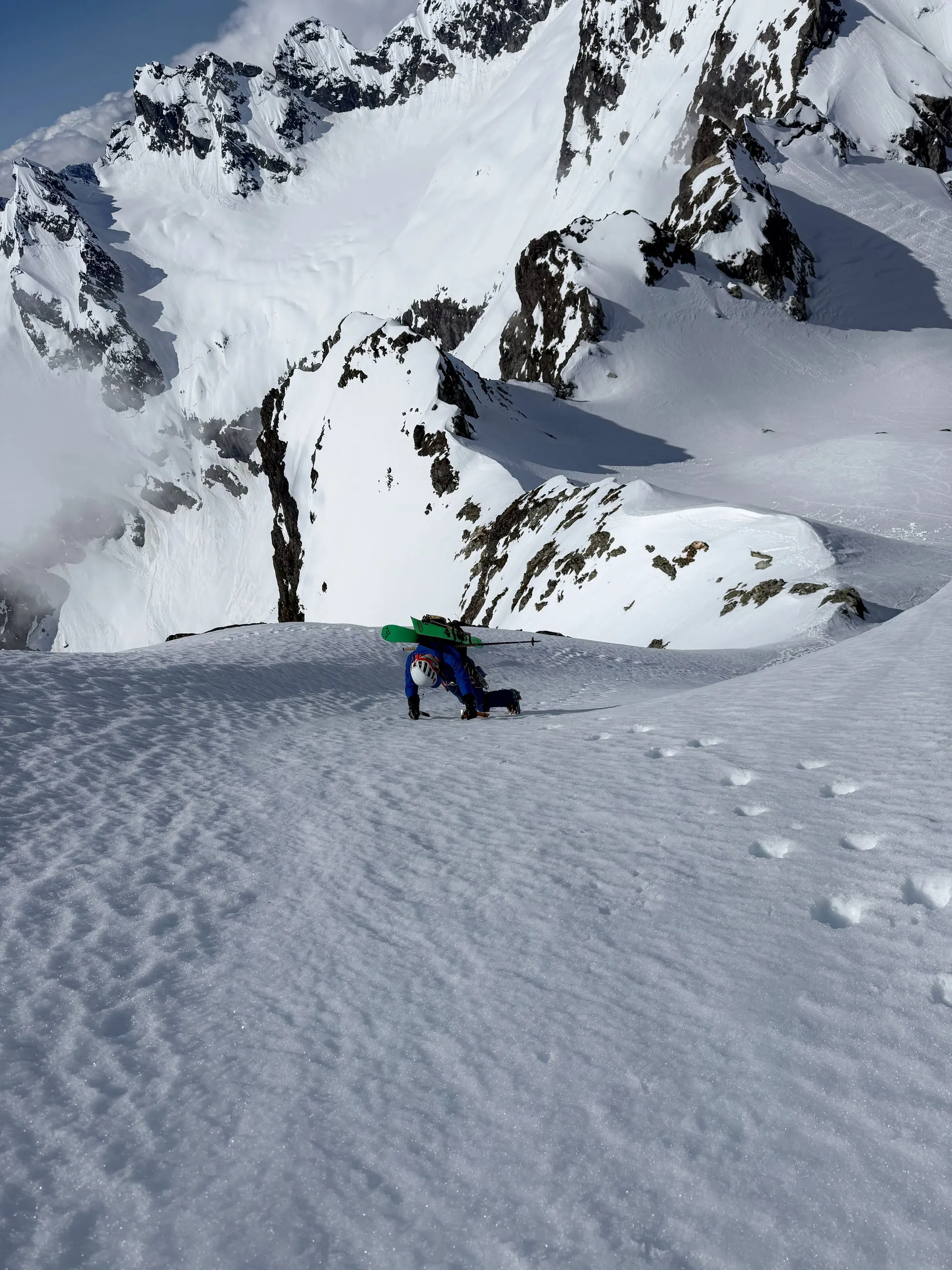 Alexis climbing firm snow toward the summit of Alpha with skis strapped to his pack