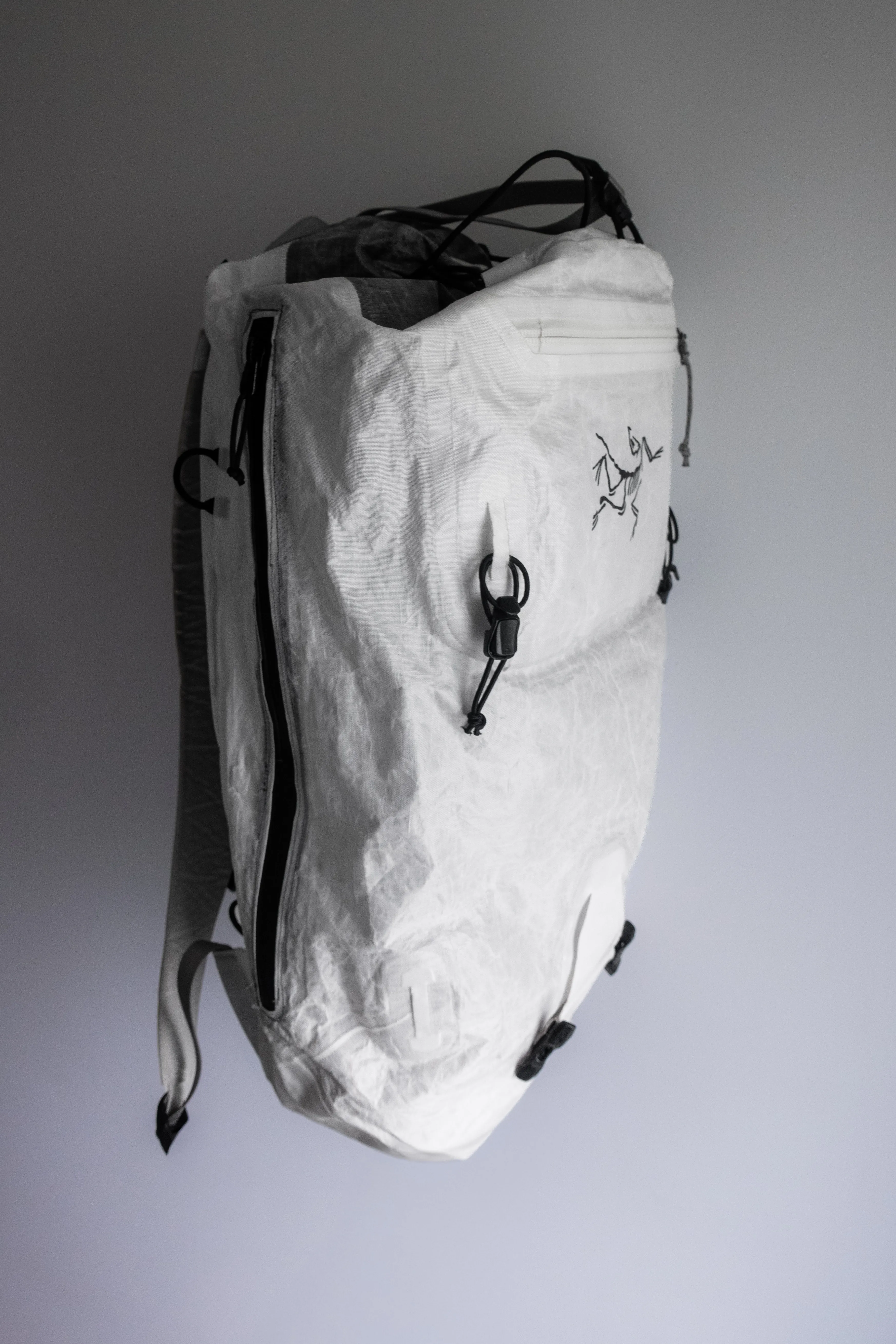 White Arc'teryx Alpha SL 30 standing against a grey wall with the added full-length side zipper visible
