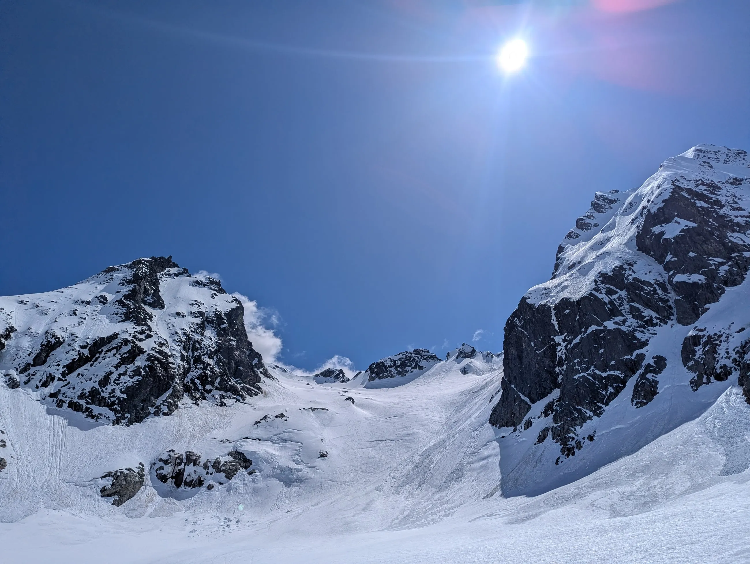 The broad snow-covered south face of Alpha Mountain between dark rock walls under a high spring sun