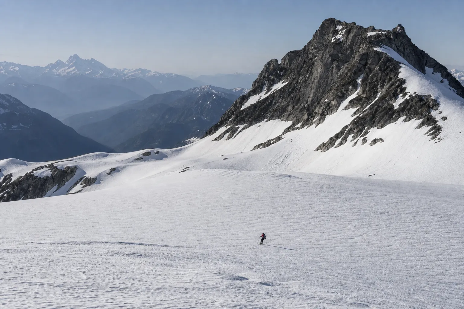 A ski alpinist crossing a broad glacier below dark granite peaks in the Coast Mountains