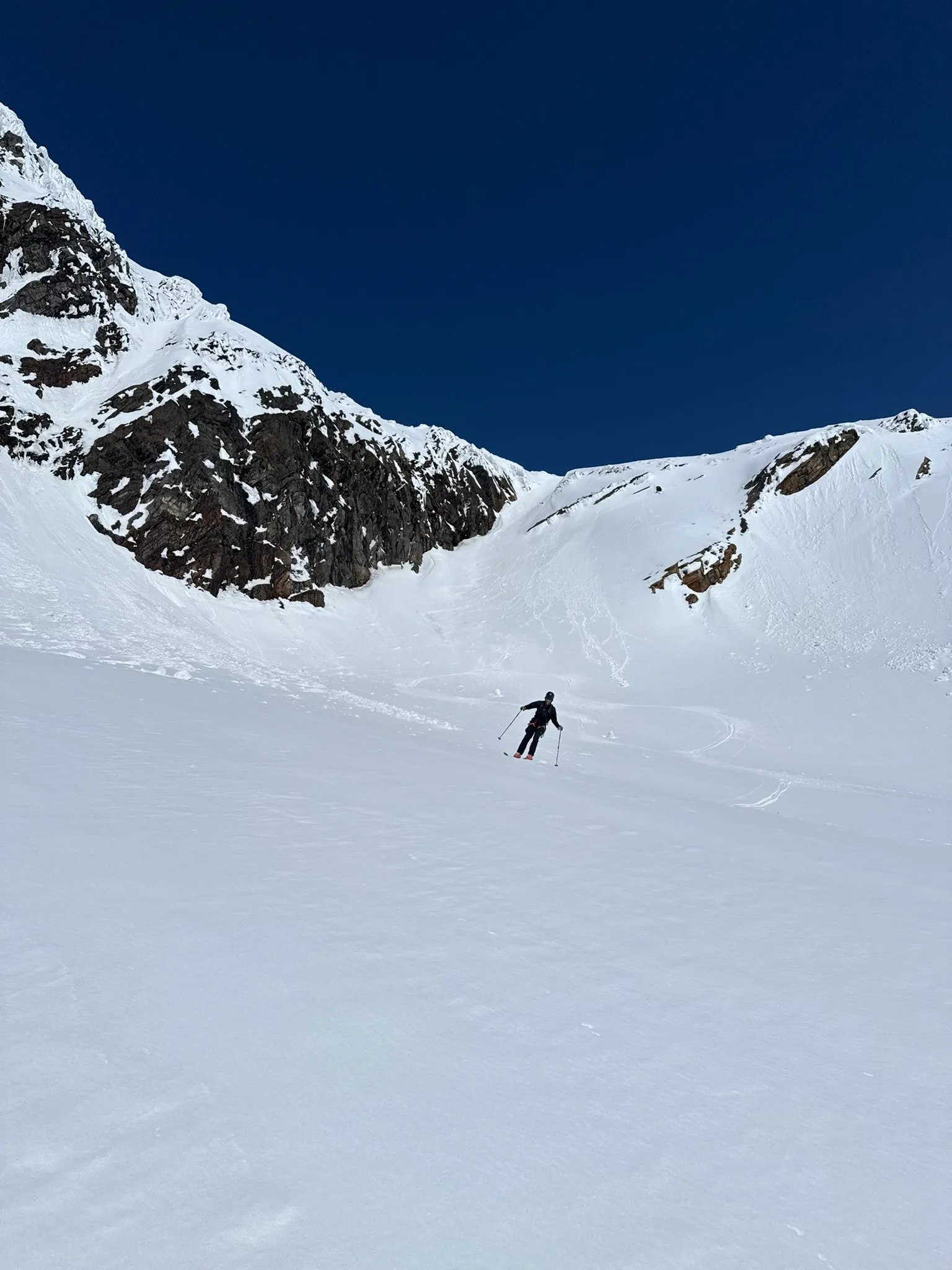 Chris skiing spring corn beneath rock walls in the hidden bowl behind the exposed ridge