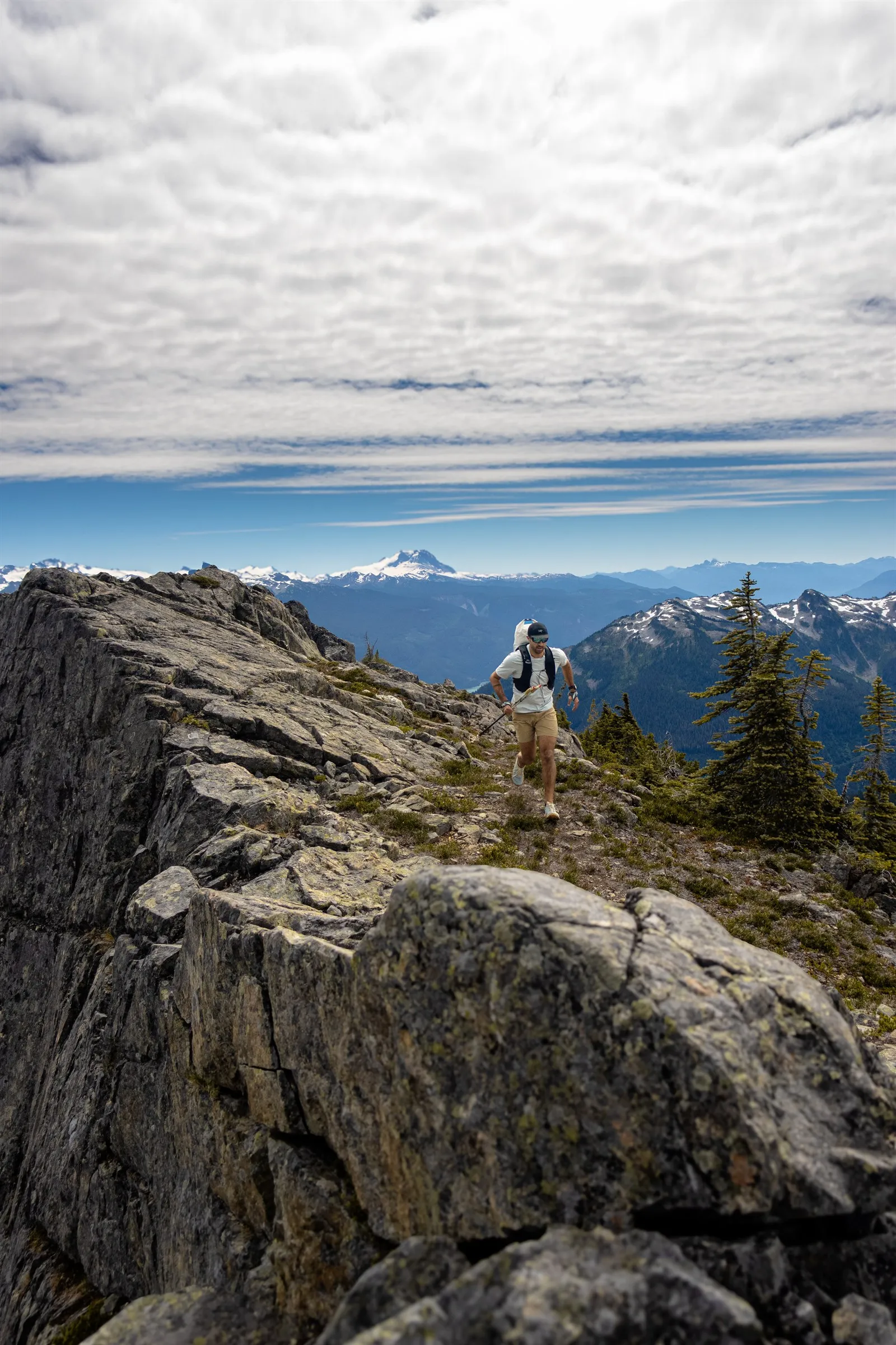 Jordan running along the rocky ridge above Brandywine Meadows with distant glaciated peaks behind him