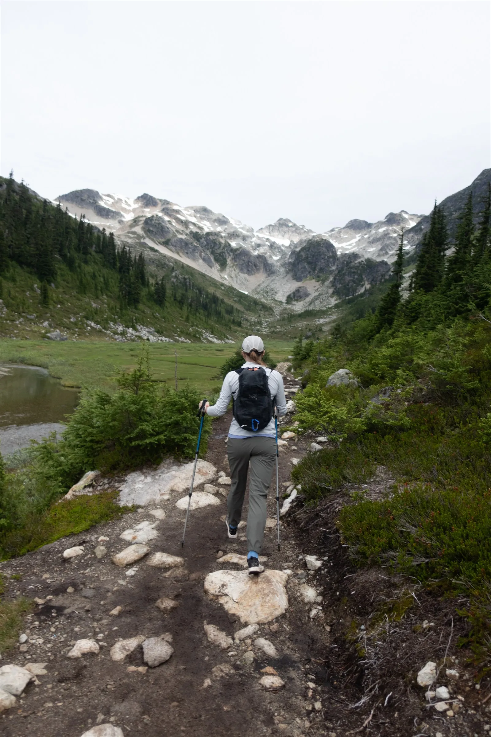 Linsey hiking with poles along the trail into Brandywine Meadows beneath snow-streaked peaks