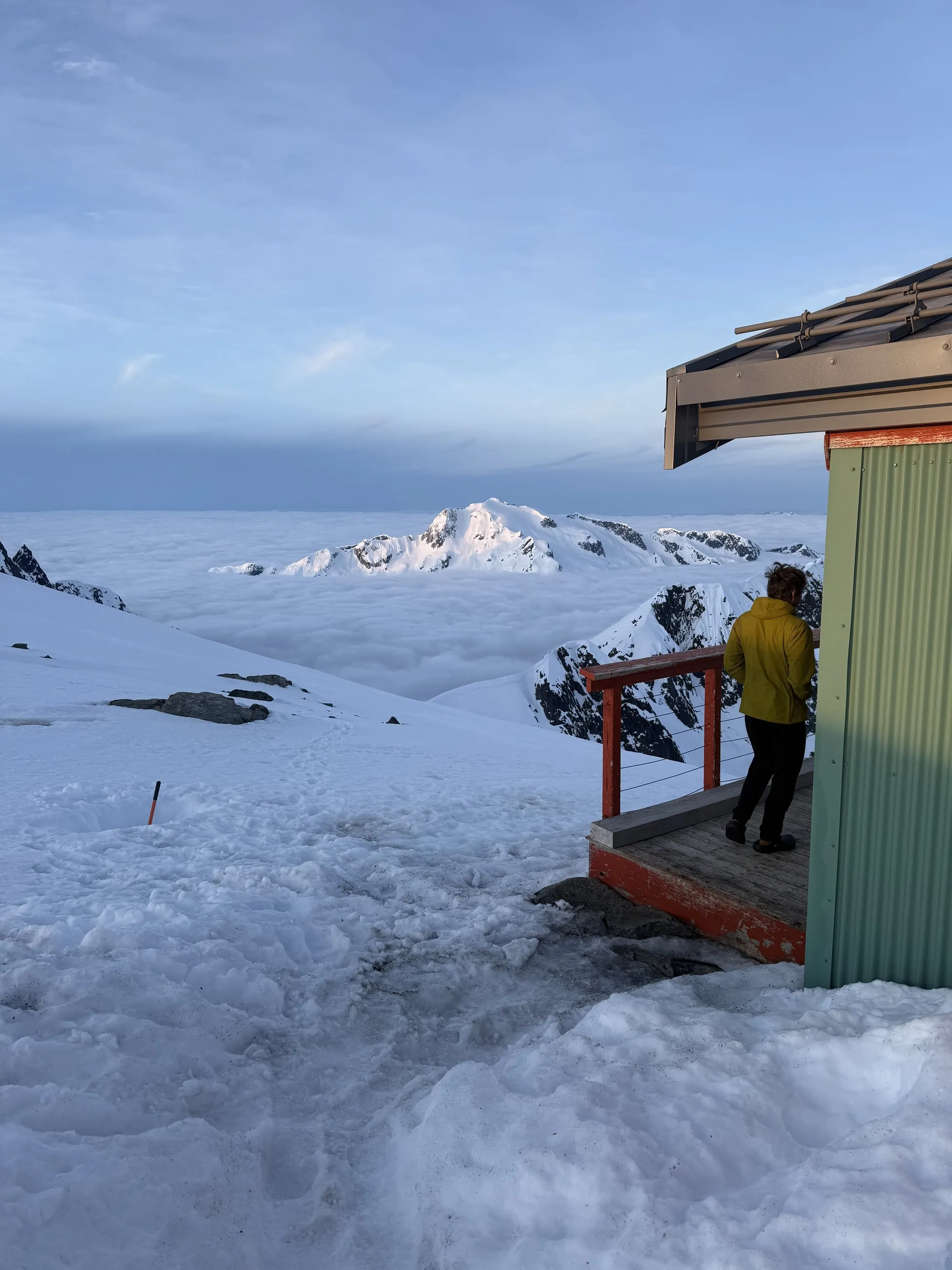 Jordan standing outside the Jim Haberl Hut above a sea of clouds at sunrise