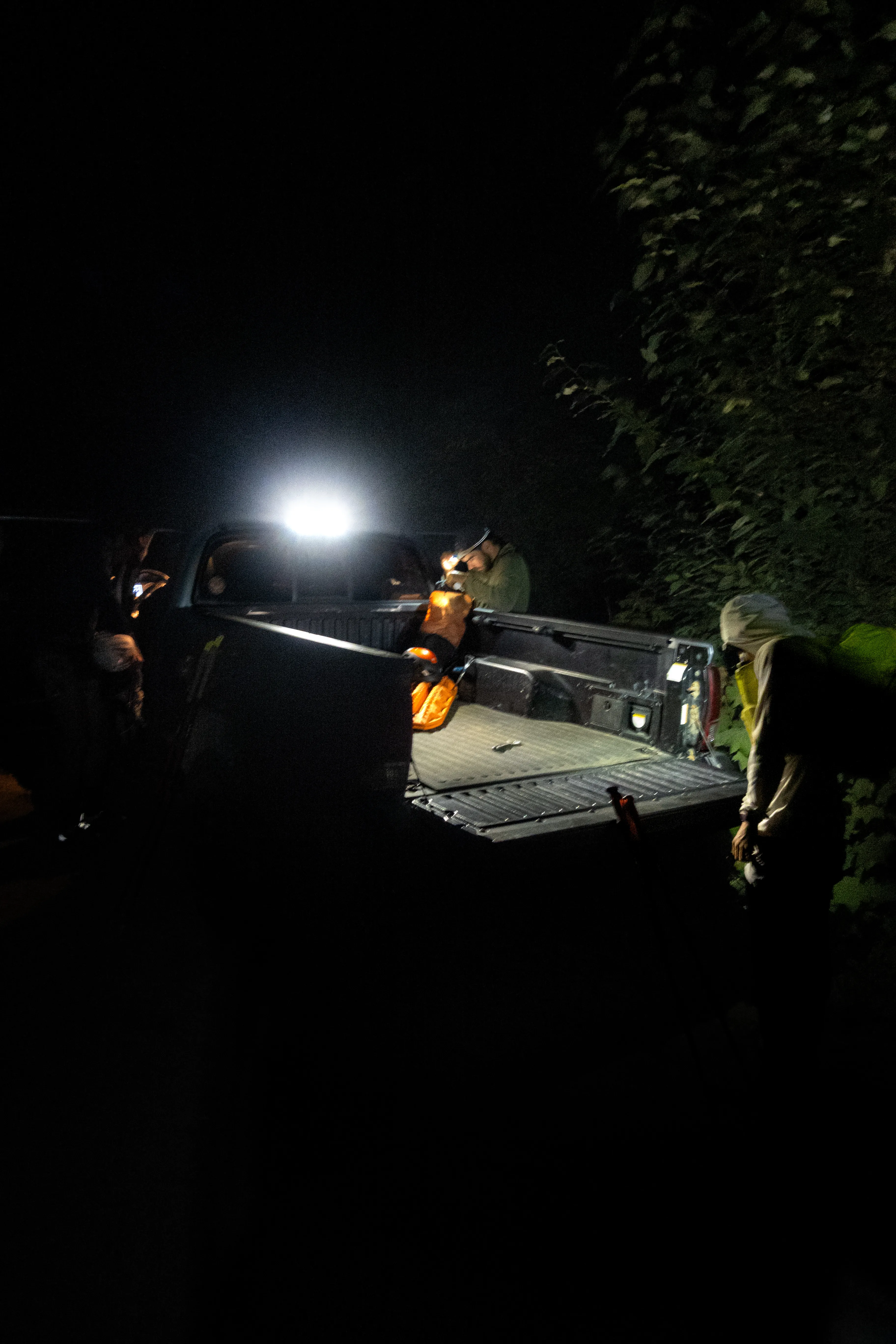 Four climbers packing equipment beside a pickup truck at the dark Sigurd Creek trailhead