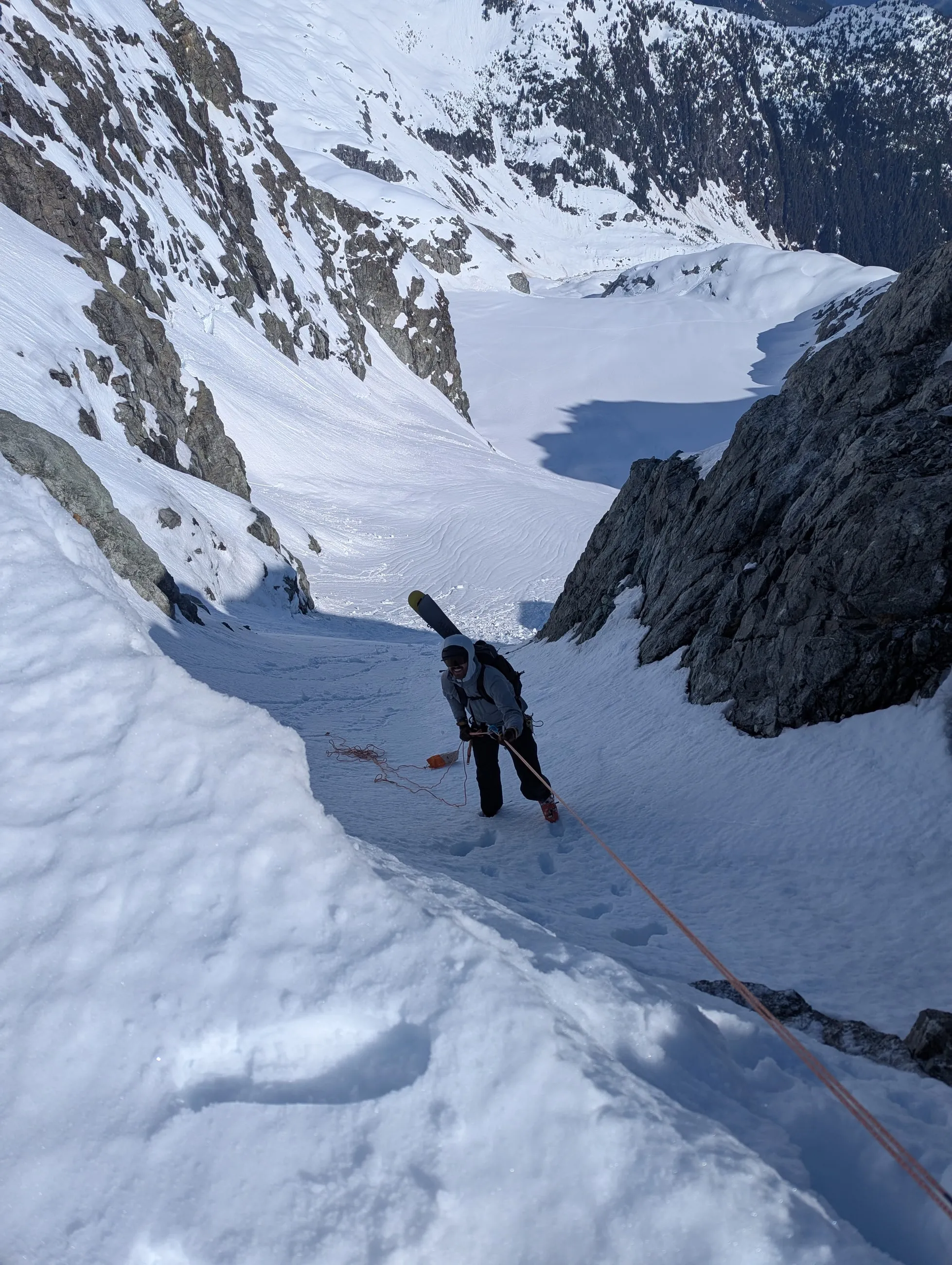 Alexis rappelling a steep snowy gully from the Alpha–Serratus col with the basin far below