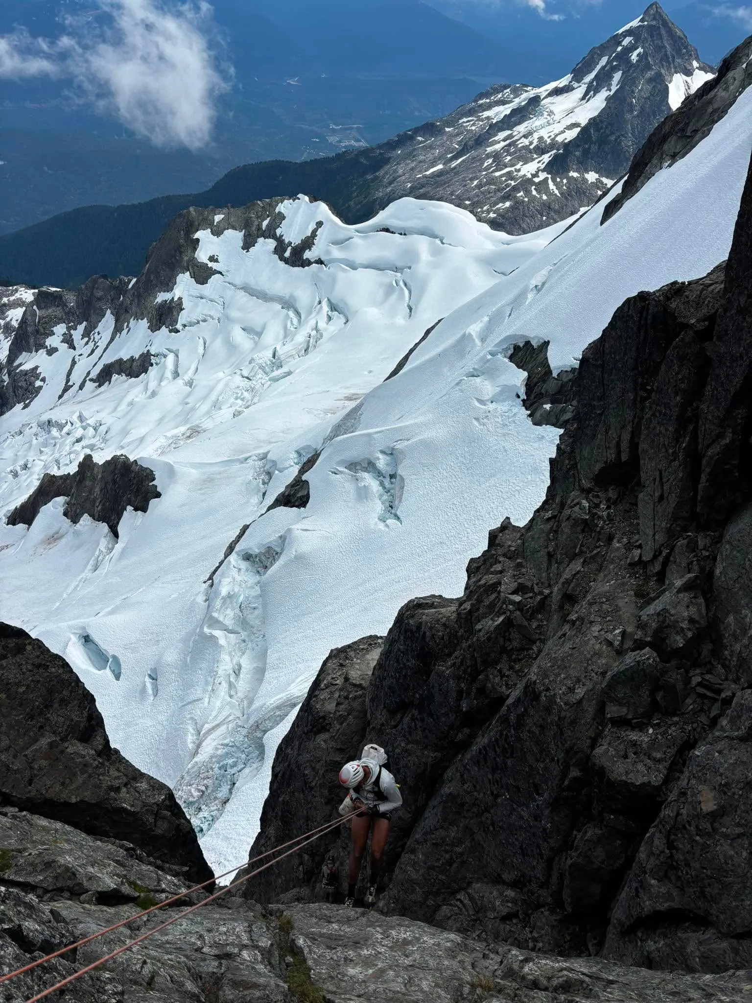 A climber rappelling a steep rock step below Mount Tantalus with a broken glacier far below