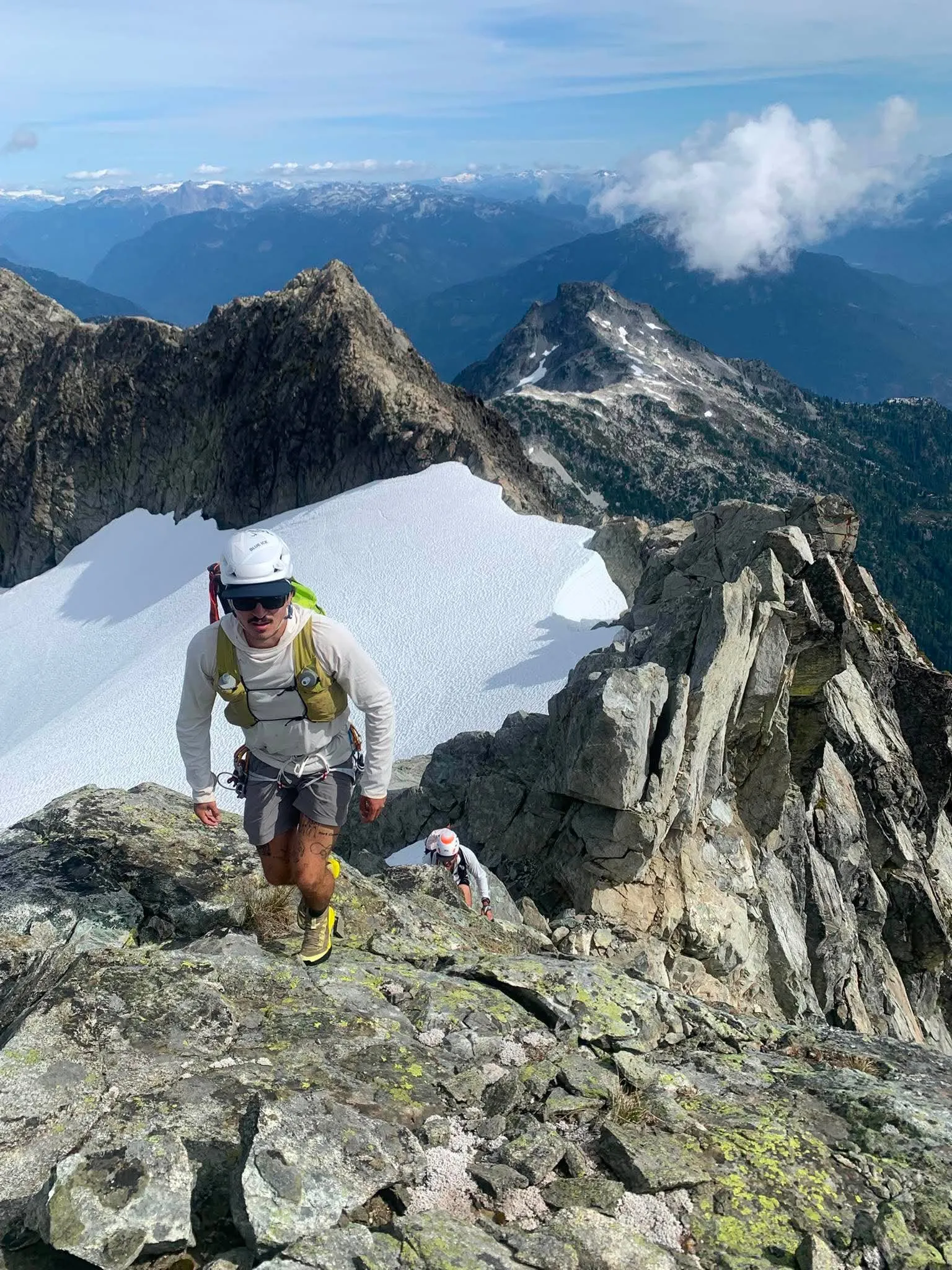 Two climbers scrambling upward on the rocky summit ridge of Mount Tantalus above summer snow