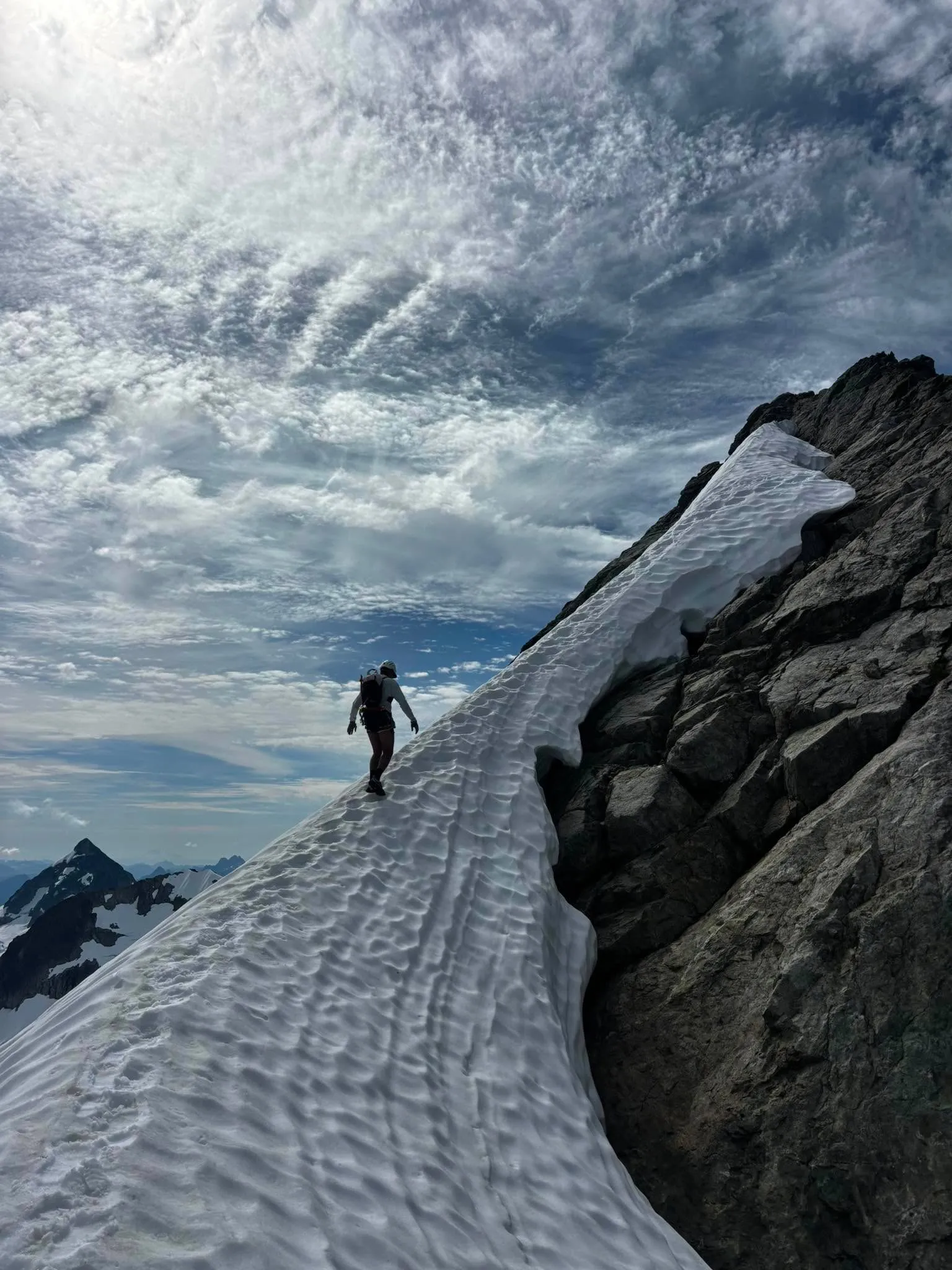 A climber traversing a narrow snow bridge attached to the rocky ridge of Mount Tantalus