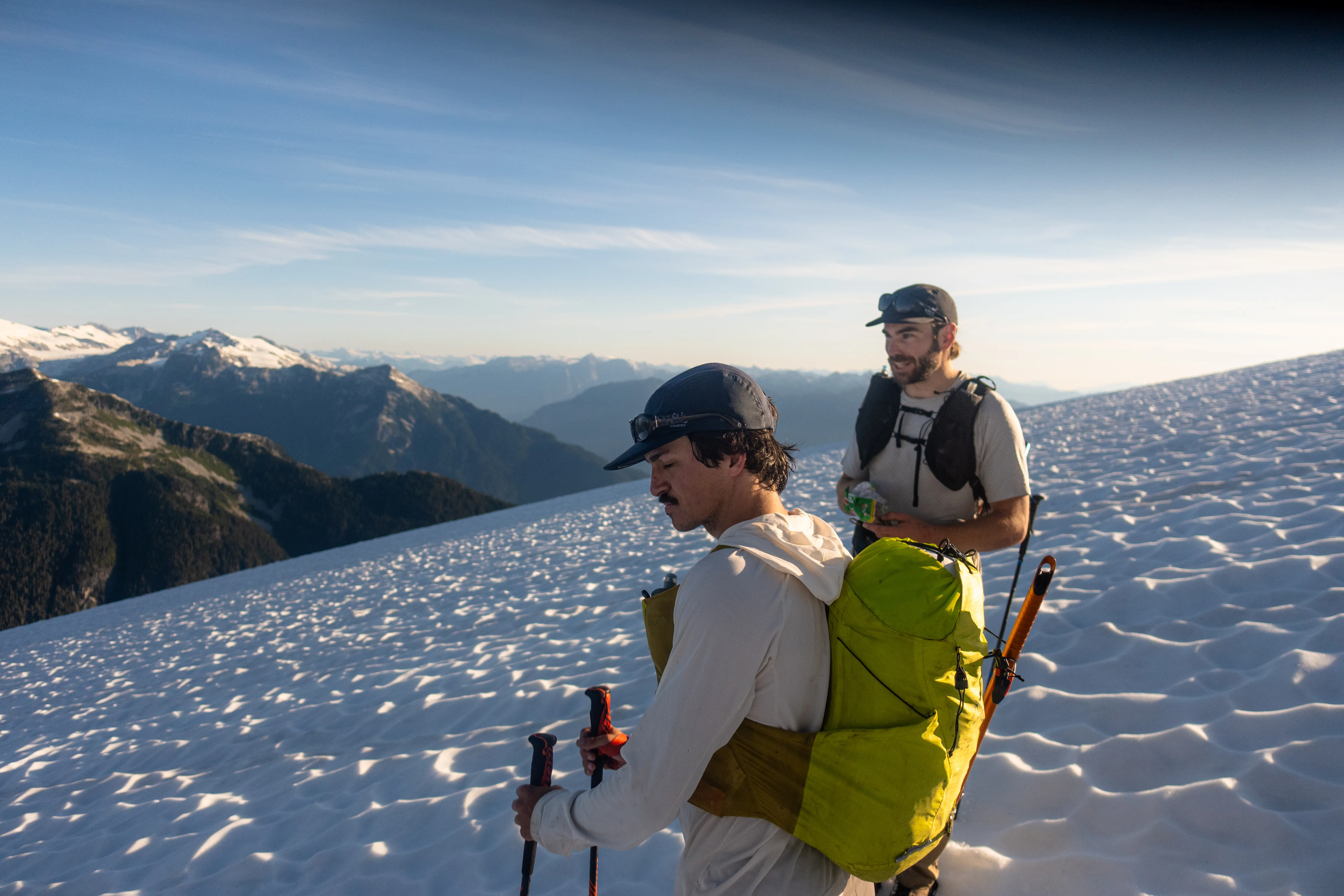 Two members of the team pausing on sunlit snow high in the Tantalus Range