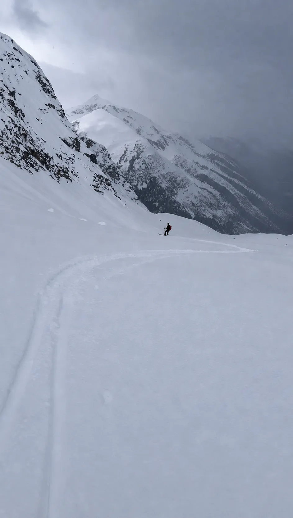 Chris skiing variable snow beneath dark rock walls during the descent from high on the ridge