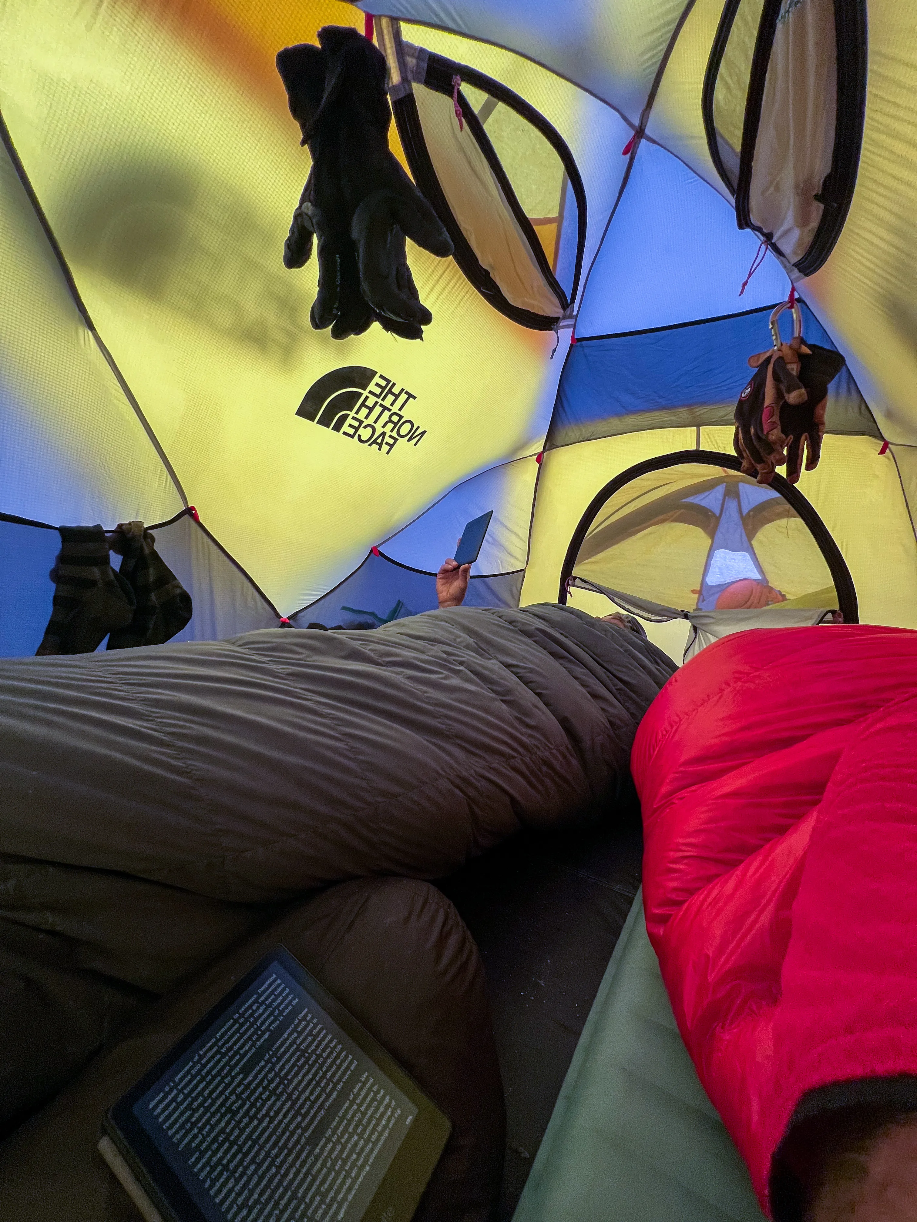 Sleeping bags, climbing gear and an e-reader inside a yellow tent during a storm