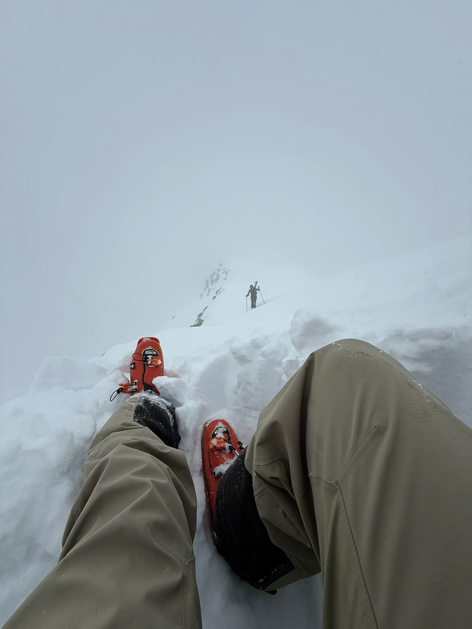 Jordan sitting in a ledge dug into the snow for shelter during a whiteout high on the ridge