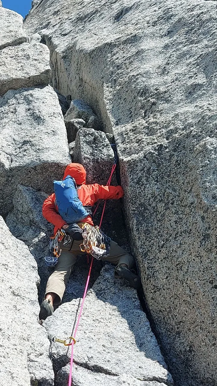 Chris climbing between wide granite cracks on the upper Beckey–Chouinard